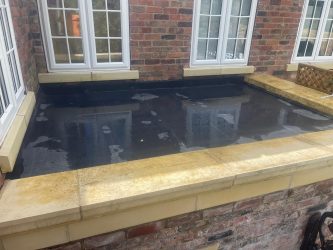 Flat rubber roof over a bay window enclosed by stone-coped parapet walls